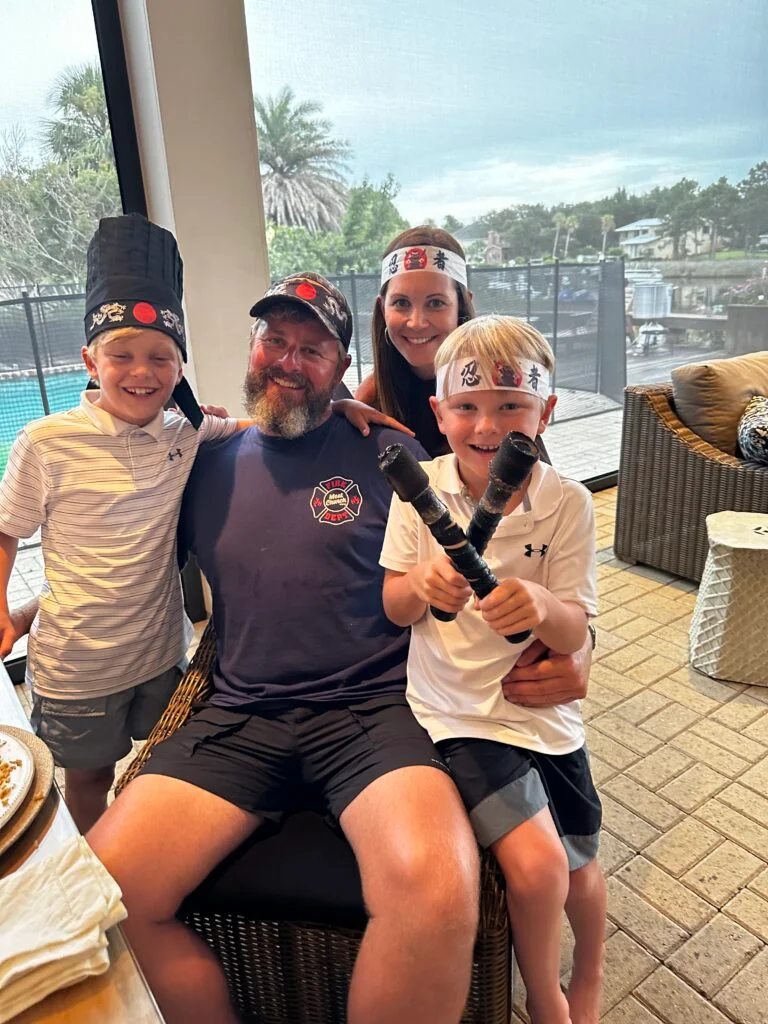 Family of four smiling and wearing Hibachi-themed headbands, posing together after a private Hibachi experience